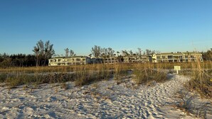 Un hotel frente a la playa con varias construcciones, una playa arenosa y vegetación escasa.