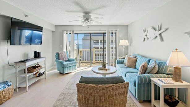 A living room with a ceiling fan, a TV, a sofa, a coffee table, and a view through a glass door to the outside. - Grove Pointe 303-2BR/2BA-2nd Row-Oceanview (North Myrtle Beach)
