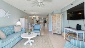 A living room with a ceiling fan, a TV, and a dining area in the background. - Grove Pointe 303-2BR/2BA-2nd Row-Oceanview (North Myrtle Beach)
