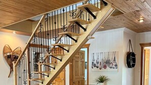 Amplia sala de estar con una escalera de madera, un sofá rojo, una pequeña mesa con una planta y un estante en la pared con objetos decorativos.
