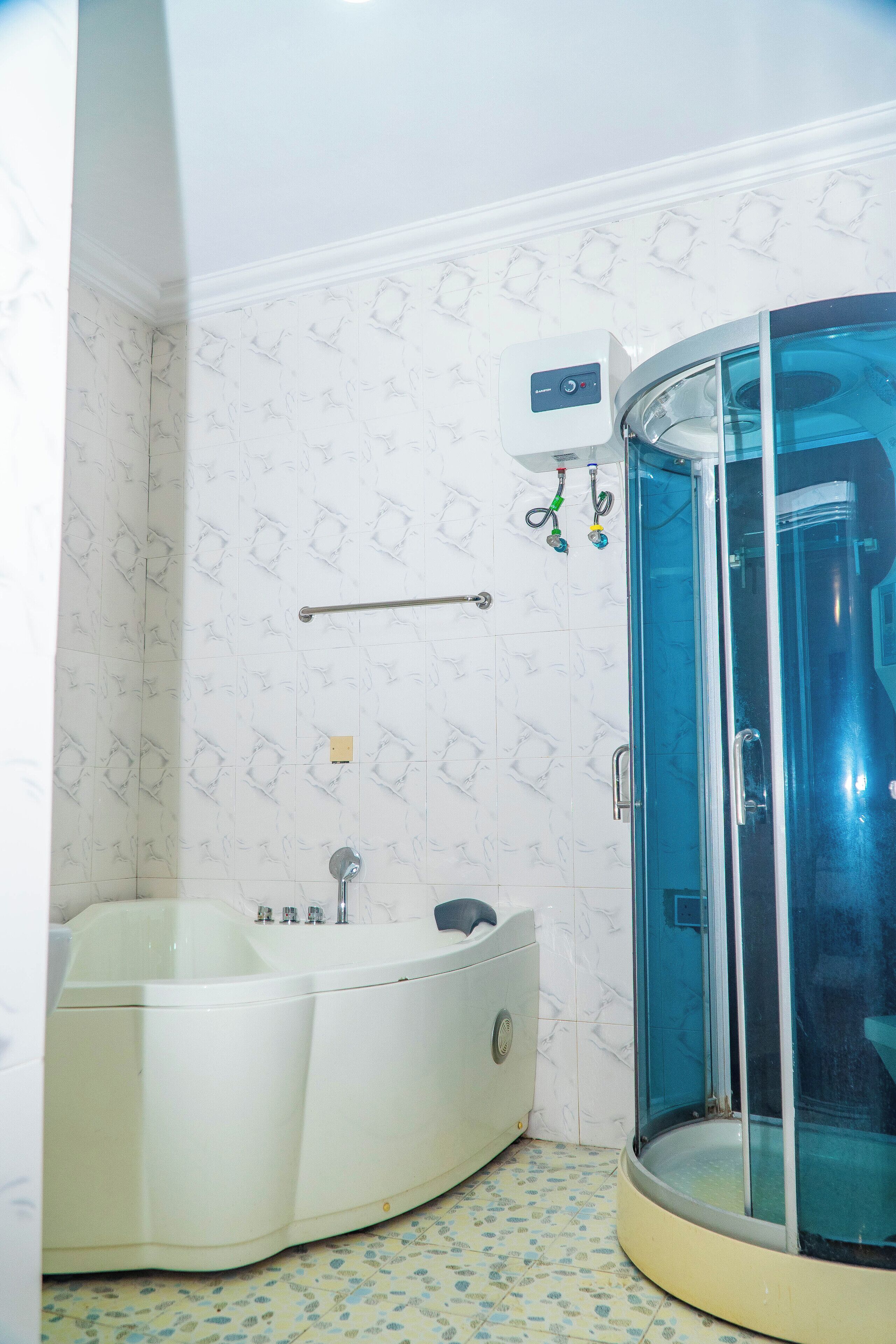 A bathroom with a glass-enclosed shower, a white bathtub, and patterned tiles.