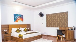 A hotel room with a bed, bedside table, desk, chair, and artwork on the wall. - Ringruby Hotel, United Estate (Lekki)