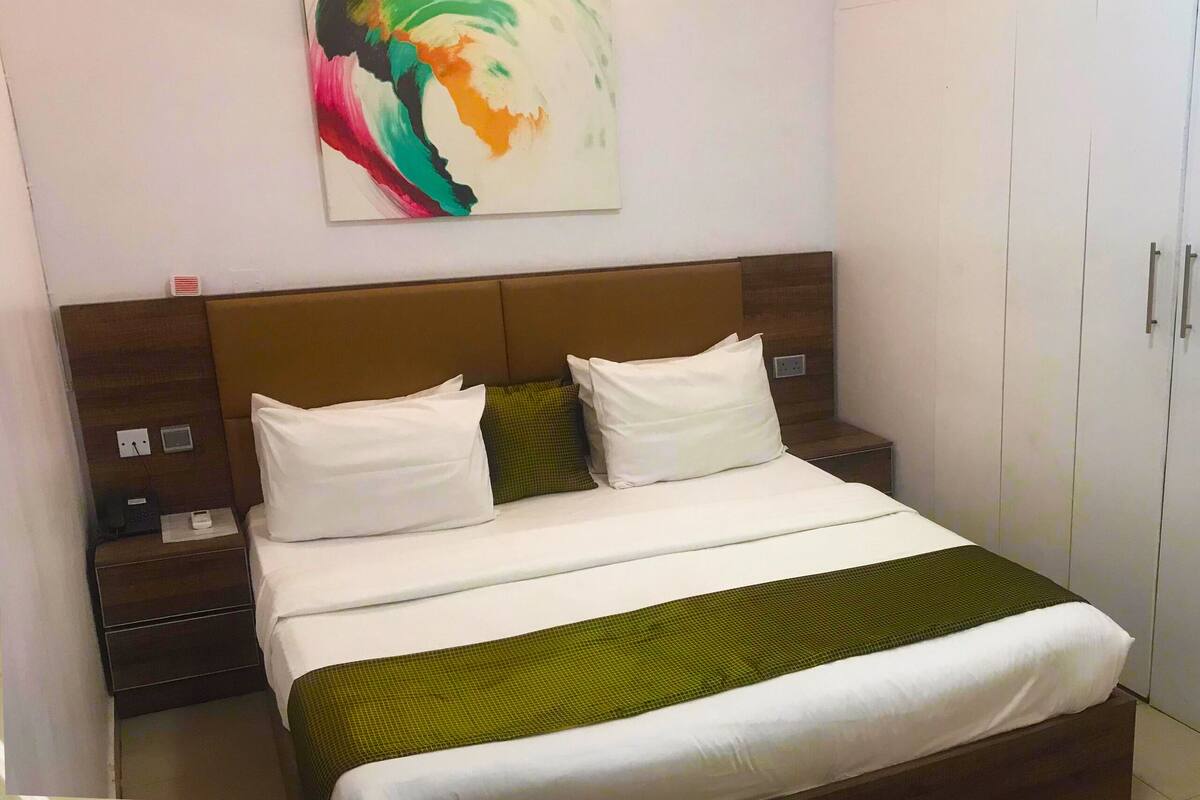 A hotel room with a bed, a nightstand, a wardrobe, and a painting on the wall.
