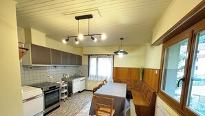 A compact kitchen with a dining area, featuring a stove, sink, and wooden cabinets. - Le Gîte de Pipala *** (Mittlach)