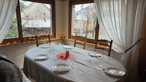 A dining table set for six with candles, glasses, and plates, surrounded by windows with curtains and string lights. - Le Gîte de Pipala *** (Mittlach)