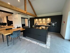 Una cocina moderna con armarios oscuros, una mesa de comedor de madera y una isla grande.