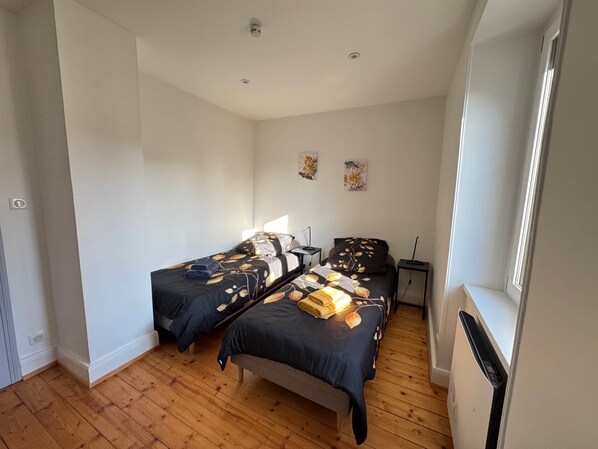 Un dormitorio con dos camas, suelo de madera, un radiador y obras de arte en la pared.