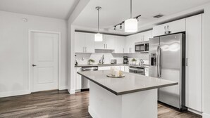 A modern kitchen with white cabinetry, a central island, stainless steel appliances, and a wooden floor. - Comfort & Convenience: 2BR Unit with Free Parking! (Miami)
