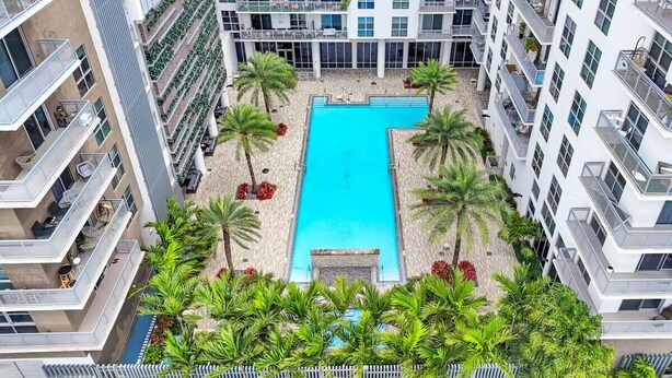 A high-rise building with a central swimming pool surrounded by palm trees and outdoor seating areas. - Comfort & Convenience: 2BR Unit with Free Parking! (Miami)