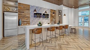 A modern kitchen with a wooden accent wall, a stainless steel refrigerator, and a bar area with stools. - Comfort & Convenience: 2BR Unit with Free Parking! (Miami)