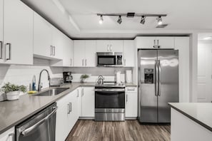 A modern kitchen with stainless steel appliances, white cabinetry, and a wooden floor.