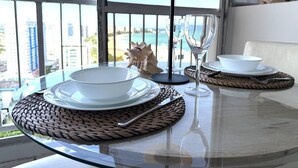 Une table à manger offrant une vue sur la ville et l’océan, une lampe et un coquillage décoratif.