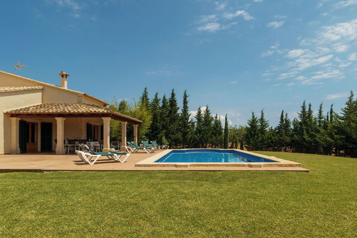 A house with a swimming pool, a patio with lounge chairs, and a covered area with a table and chairs.