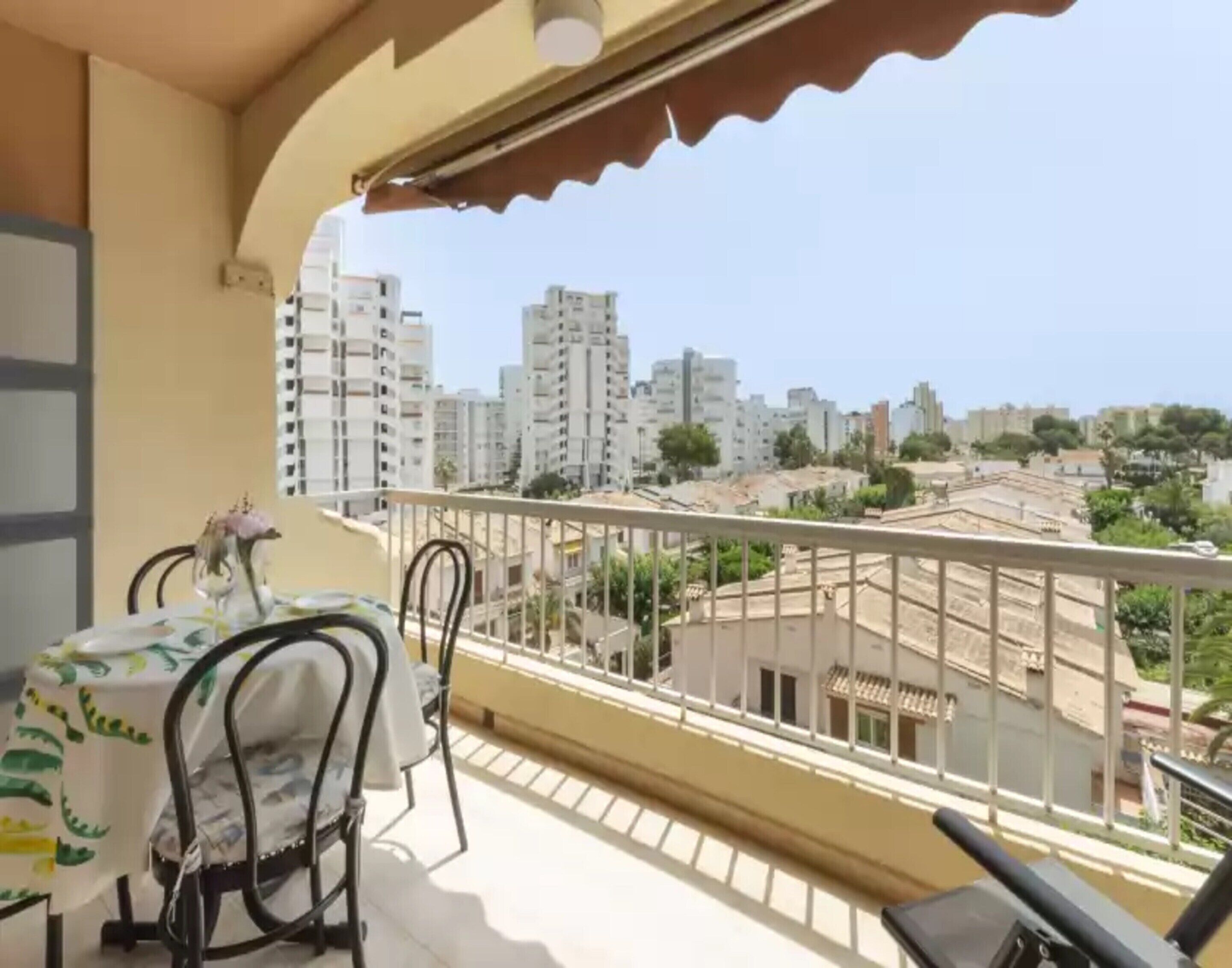 A balcony with a table and chairs, overlooking a cityscape with high-rise buildings.