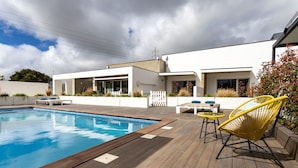 A modern outdoor pool area with a wooden deck, a white building, and yellow chairs.