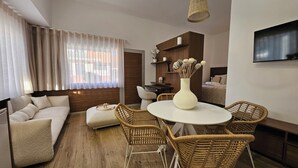 A modern living room with a round dining table, wicker chairs, a sofa, and a TV mounted on the wall.