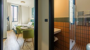 A modern hotel room with a dining area, a bathroom with a glass shower, and a view of the city. - Cozy and Central Studio in Bovisa, Milan (Milan)