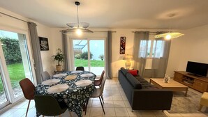 A modern living room with a dining area, large windows, and a television. - Apartment in Carantec Near Sandy Beaches (Carantec)