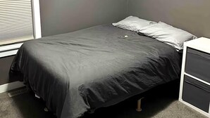 Een slaapkamer met een enkel bed, een nachtkastje en een raam met jaloezieën.