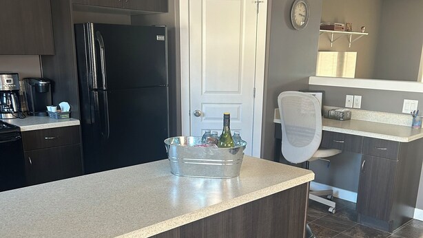 Een moderne keuken met donkerhouten kasten, een zwarte koelkast, een koffiezetapparaat en een klein eilandje met een fles.