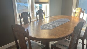 Een eetruimte met een ronde houten tafel, omringd door zes stoelen, elk met een kussen met een bladmotief.