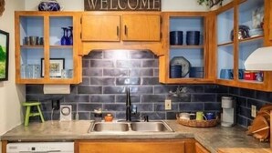 A kitchen with wooden cabinets, a black tiled backsplash, and a welcome sign. - The Ace, 1BR King Duplex by Velvet Ditch Villas (Oxford)