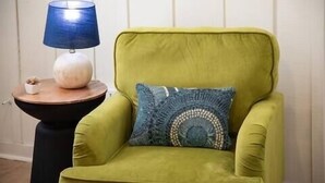 A green armchair with a blue and white patterned pillow, a round wooden side table with a blue lamp, and a small white bowl with items on it. - The Ace, 1BR King Duplex by Velvet Ditch Villas (Oxford)