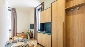 Une pièce compacte comprenant un coin cuisine, un espace repas avec une table dressée pour deux personnes et un canapé.