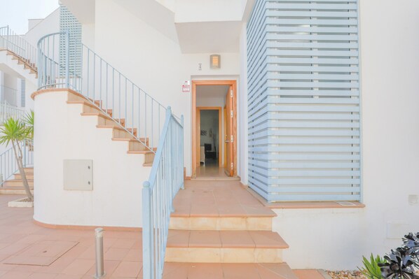 A staircase leading to a door, a metal railing, and a building facade with horizontal slats.