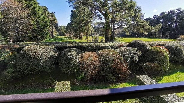 A well-maintained garden with neatly trimmed hedges and a variety of trees, including tall conifers and deciduous trees. - T2 cosy - Vue Golf - Proche Plage (Pornic)