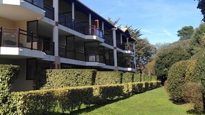 A multi-story building with balconies, a well-maintained lawn, and neatly trimmed hedges. - T2 cosy - Vue Golf - Proche Plage (Pornic)