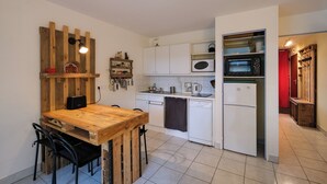 A compact kitchen with white cabinets, a wooden dining table, and a microwave. - T2 cosy - Vue Golf - Proche Plage (Pornic)