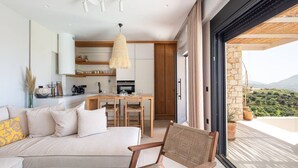 Ein modernes Interieur mit einer Couch, einem Esstisch, Stühlen, einer Küchenzeile und Blick auf eine Berglandschaft durch große Fenster.