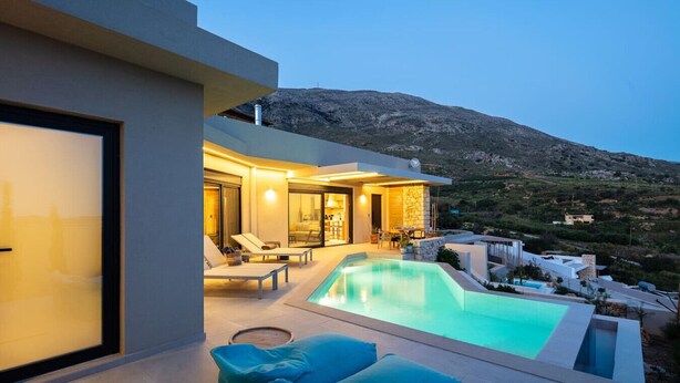 Ein modernes Haus mit Swimmingpool, einer Terrasse mit Liegestühlen und Blick auf die Berge.