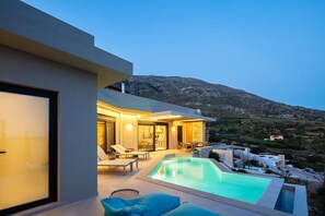 Una casa moderna con piscina, un patio con sillones y vistas a la montaña.