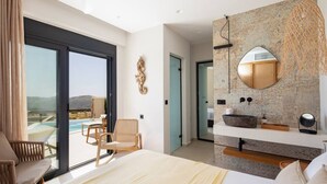 Ein modernes Hotelzimmer mit einem großen Bett, einem Badezimmer mit Waschbecken aus Stein, Blick ins Freie und einem Balkon mit einem Stuhl.