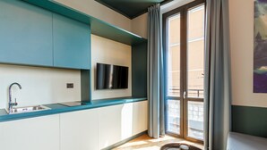 Een kleine keuken met een ingebouwde gootsteen, een flatscreen televisie en een raam met gordijnen.