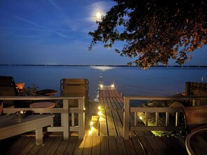 A wooden deck with a view of a calm body of water at dusk, a dock extending into the water, and outdoor seating. - 10 out of 10 for Waterfront 2-bdrm Cottage on Grand Lake w/Seasonal Fishing Pier (Celina)