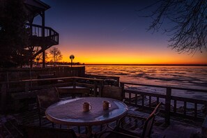 A sunset view from a waterfront patio with tables and chairs, overlooking a body of water. - 10 out of 10 for Waterfront 2-bdrm Cottage on Grand Lake w/Seasonal Fishing Pier (Celina)