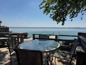A deck with a round glass table and chairs, overlooking a calm body of water. - 10 out of 10 for Waterfront 2-bdrm Cottage on Grand Lake w/Seasonal Fishing Pier (Celina)
