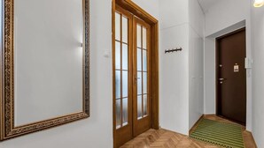 Un couloir doté d’un plancher en bois, d’un paillasson vert et d’une porte en bois avec des panneaux de verre.