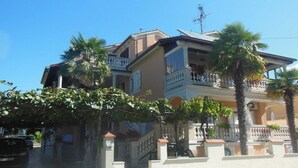 Une maison à plusieurs étages, dotée de balcons, d’une entrée sécurisée par un portail et bordée de palmiers.