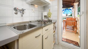 Une cuisine équipée d’un évier à deux bacs, d’une cuisinière et d’une machine à café. Une chaise en bois et une table se trouvent à l’extérieur de la porte.