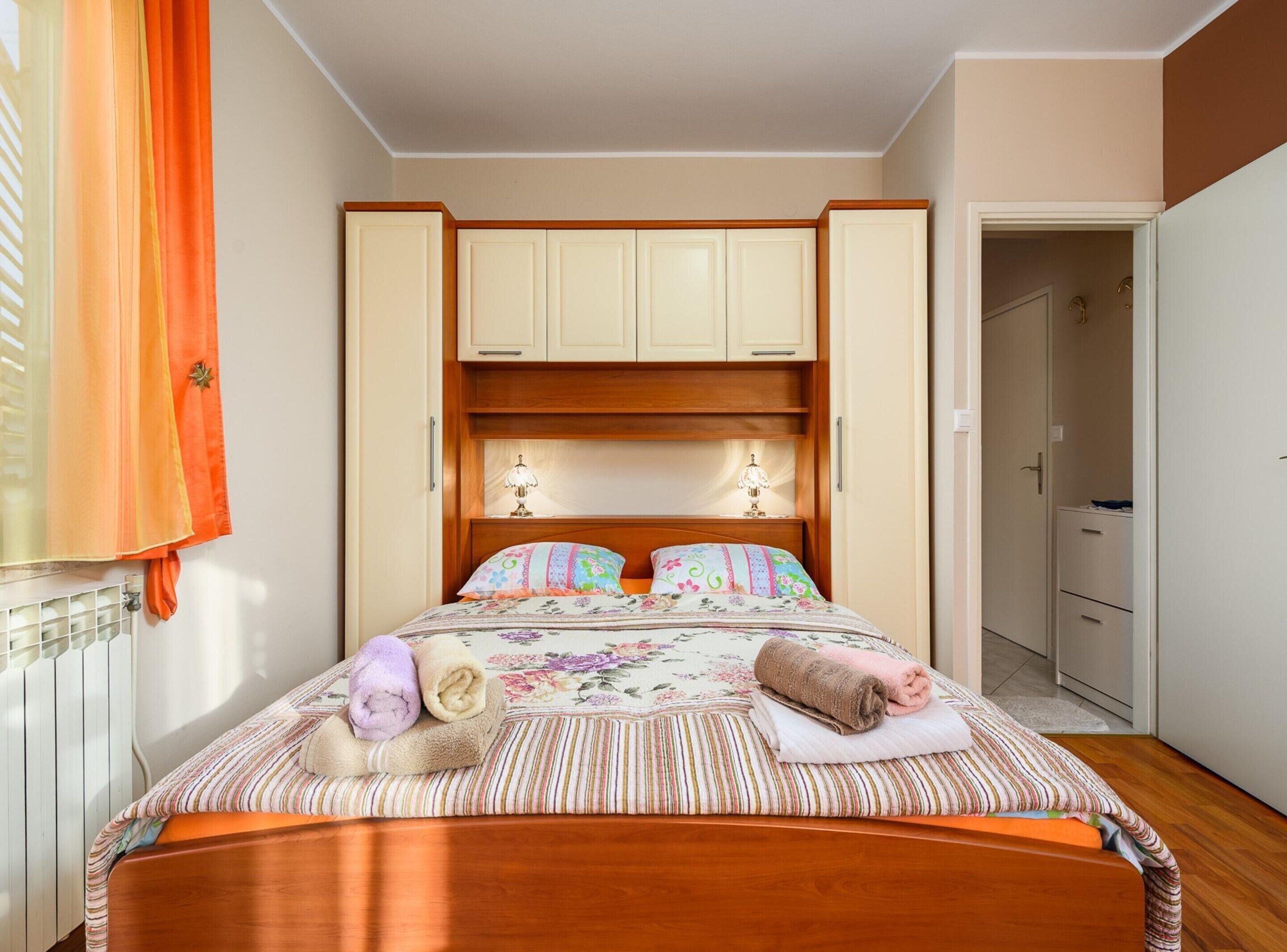 A bedroom with a wooden bed, a nightstand, a dresser, and a window with curtains.