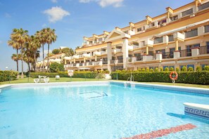 A swimming pool with a clear blue water, surrounded by a building with balconies and palm trees. - Studio in Marbella Near Romana Playa Beach (Marbella)