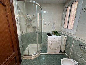 A bathroom with a glass-enclosed shower, a washing machine, a radiator, and a sink. - Rooms Valencia (Barcelona)