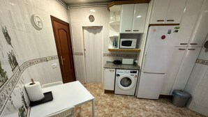 A compact kitchen with a washing machine, microwave, and refrigerator. - Rooms Valencia (Barcelona)
