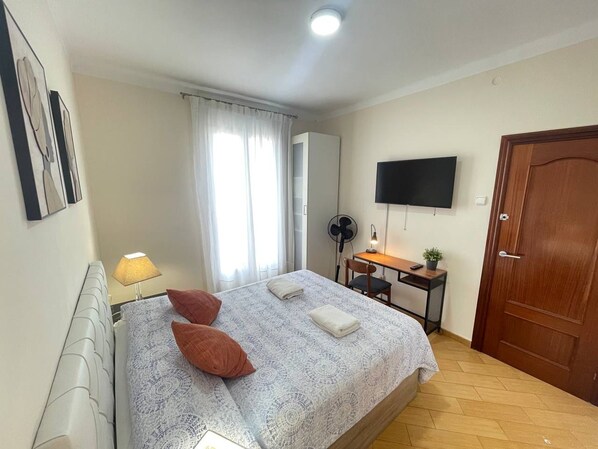 A bedroom with a bed, a desk, a chair, a TV, and a door.