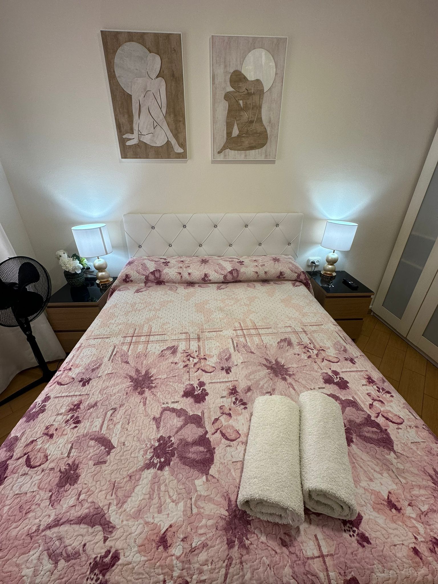 Una habitación de hotel con una cama grande, dos mesitas de noche con lámparas, una silla y dos obras de arte en la pared.