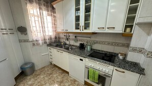 A kitchen with white cabinets, a granite countertop, a sink, a stove, and a trash bin. - Rooms Valencia (Barcelona)